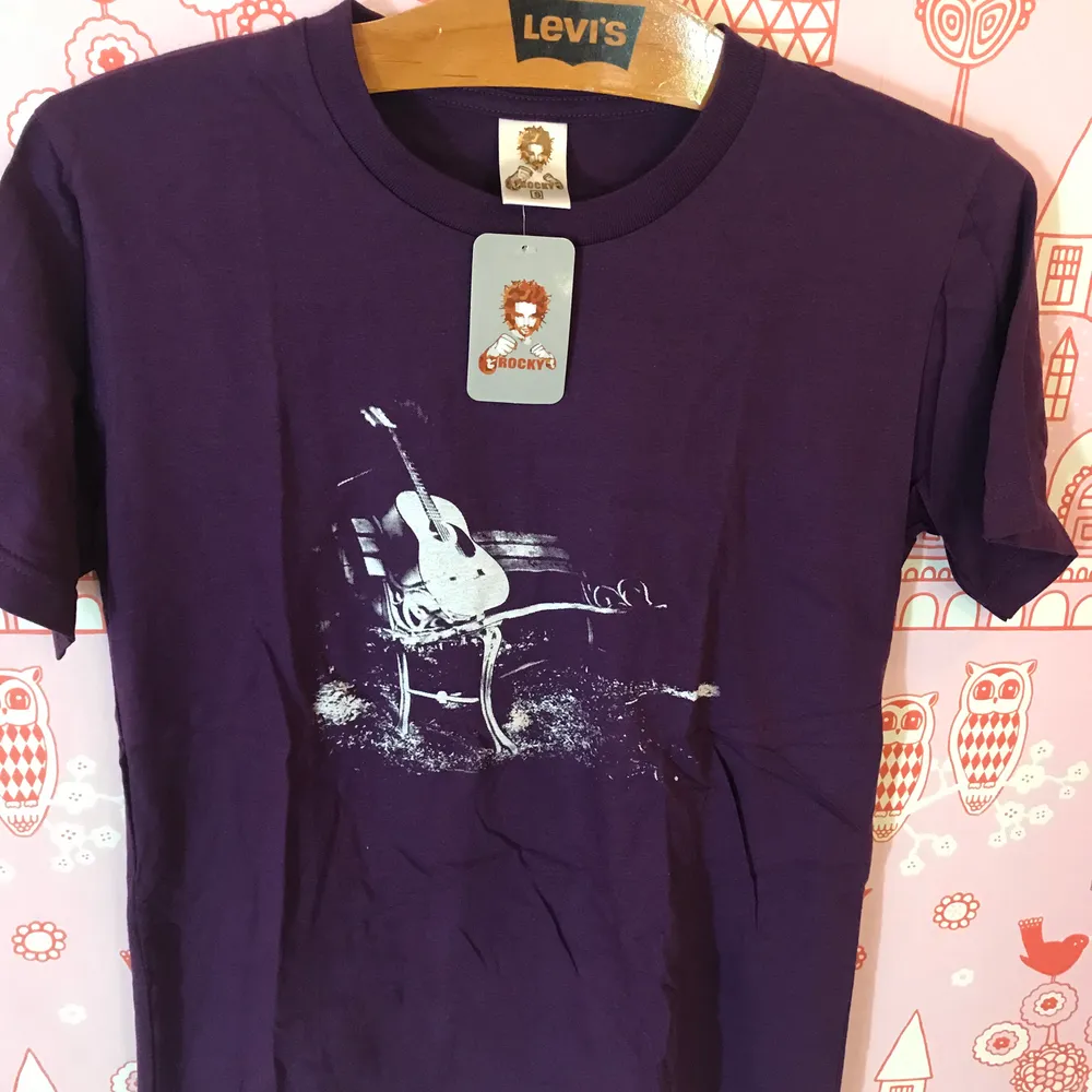 Lila T-shirt med gitarr i storlek S. Mäter 60cm på längden och 44cm på bredden. Hämtas gärna i Enskededalen.. T-shirts.