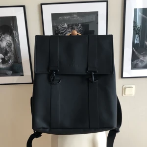 Svart ryggsäck Rains - En stilren ryggsäck i regnsäkert material. Ficka för dator. 