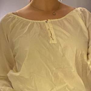 En vit skjorta med 3 små knappar vid bröstet och volangliknande detaljer vid slutet av armarna