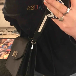  - En svart väska med vit och svart randigt band. Extremt lätt att styla då den passar till alla outfits. Nypris va 400 och säljer för 75kr frakten står köparen för om du inte kan mötas upp :)