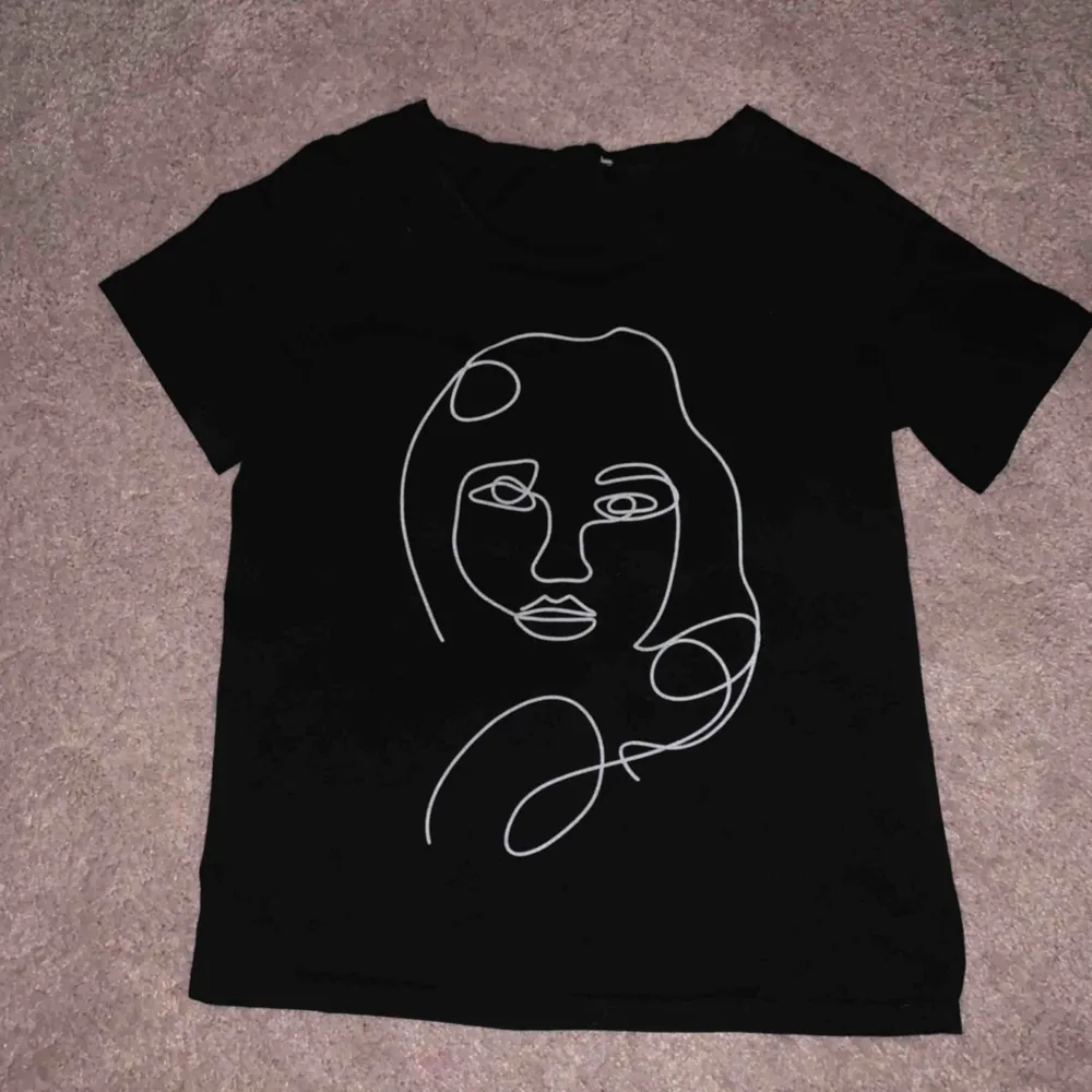 En t-shirt men ett ansikte på, t-shirten är svart med ett vitt tryck . T-shirts.