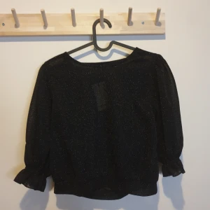 Glittrig topp från Bikbok - Populär glittrig topp med lite puffiga axlar/ärmar från bikbok i strl s. Toppen är i lätt genomskinligt tyg. Oanvänds med lappen kvar. Nypris 249:- säljes då jag inte tyckt modellen passade mig. Köparen står för frakt.
