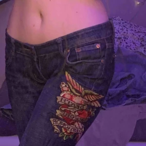 Ed Hardy Jeans - Mörkblå Jeans från Ed Hardy. Perfekt skick. Lågmidjade / mid. Broderat motiv som föreställer hjärtan och rosor och läser ”death before dishonor”. Räcker till mina fötter, jag är 1,75 m. 