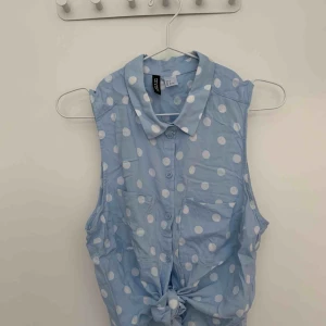  - Ljusblå kort knytblus med vita prickar.   Köparen står för porto. 