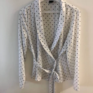 Prickig omlottopp  - En prickig wrap topp (omlottopp) från Gina Tricot. Den är jätteskön och somrig. Finns även knytdetaljer. Har aldrig använts. Säljes då jag är i behov av pengarna. 