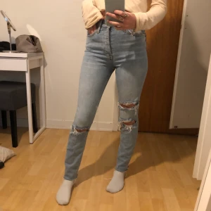 Jeans från Gina Tricot i bra skick.  - Högmidjade jeans från Gina tricot. Hål på knäna och slitningar längst ner. Det är knappar hela vägen, alltså inte gylf. Säljer för 150kr + frakt. 