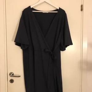 Finklänning  - En vacker klänning i ett marinblått finare tyg, med omlott, rosett och fjärilsärm! Mycket smickrande på kroppen. Använd endast en gång på ett bröllop. Ordinariepris - 699kr 