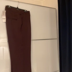 Kostymbyxor, Carin Wester  - Ett par högmidjade kostymbyxor från Carin Wester i storlek 38 som tyvärr var för stora för mig. Gjorda av ett tyg som påminner om silke. Vinröda/bruna. Lapprna och en extra knapp finns kvar. Möts upp i stockholm. Betalning sker via swish. 