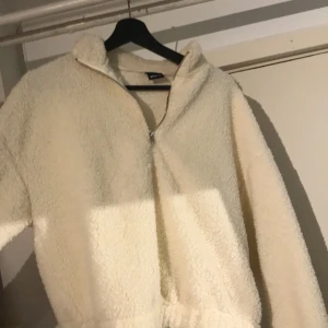 Teddyjacka - Teddytröja i krämvit färg. Storlek medium och slutar ungefär vid naveln. Polyester material. Använd ett fåtal gånger och köpt för ca 6 månader sedan. Väldigt bra skick! Inköpspris 299