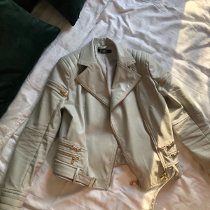 Skinnjacka - Benvit/ljus beige skinnjacka med guld detaljer. Str S, ganska smal över axlar/överarmar. Ifrån Beybey Fashion (Helene torsgårdens gamla märke) Nyskick använd vid ändast ett tillfälle. Super snygg jacka säljer ändast då den är för liten för mig.