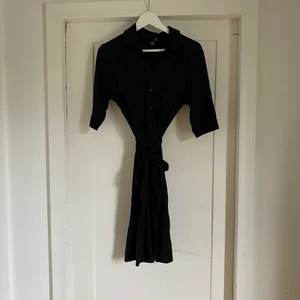 Skjortklänning svart  - Svart skjortklänning i trikå från HM. Knutans i midjan och knappar. Storlek 42, men passar en S/M. Fint skick. 