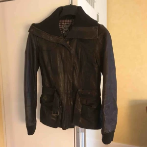  - Äkta skinnjacka som har varit i mina ägor i säkert 17 år men jag har använt den väldigt sparsam. Fint skick, det enda är ett litet hål i innerfodret på ena fickan.   Hög krage och skärp i midjan.   Köparen står för frakten.