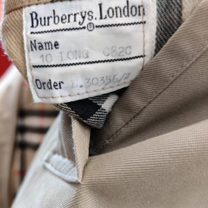 Burberry kappa - Äkta Burberry kappa inköpt hos Burberry' s i London passar både kvinnor och män. Den är i måttanpassad efter min mor som hade S i allt så måtten beskriver det men man bör vara minst 1,70 för att bär den har ett extra avtagbart tyg som smidigt sätts på/eller tas av med hjälp av en dragkedja. Använd mycket sparsamt och är i nyskick. Nypris 18 000kr