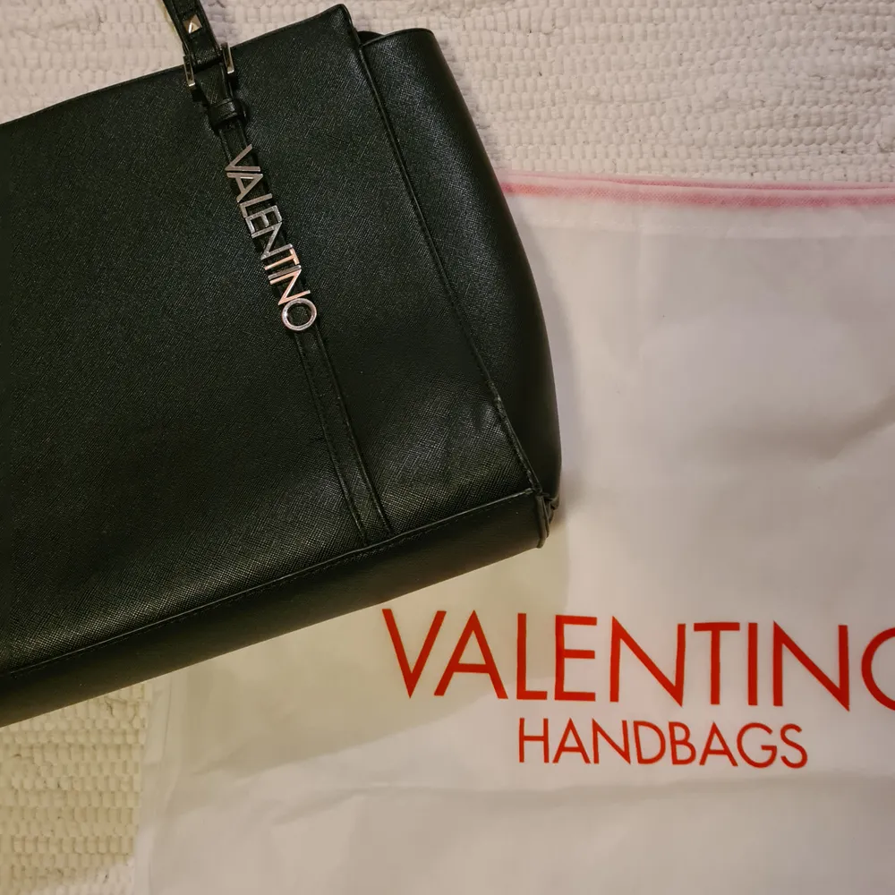 En svart Valentino handväska som har måttet 40x30cm. Nypris: 1250 kr. Den är lite sliten på något hörn, därav lågt pris. Det syns endast om man kollar noggrant. Frakt tillkommer. Betalning sker via swish:). Väskor.