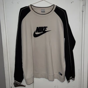 Nike sweatshirt  - Snyggt Nike sweatshirt i beige med svarta detaljer. Storlek L, sitter bra på mig med storlek M om jag viker in nederdelen. I använt men gott skick, har däremot ett litet litet hål på ena ärmen men inget man lägger märke till. Betalningen sker via Swish!