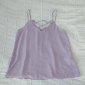 Ljuslila flowy topp/linne med smala band och knytning i ryggen - storlek 34 - Ljuslila/pastellfärgat flowy linne med smala axelband och knytning i ryggen. V-ringat och med dubbla tyger och fint fall. Bara använt en gång. Storlek 34. 