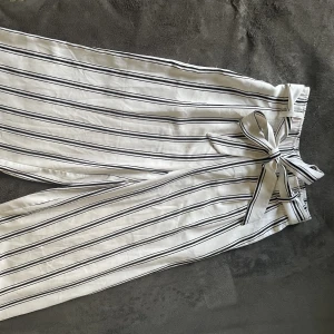 Randiga tygbyxor  - Randiga byxor i ett skönt luftigt material på benen men med resor vid midjan samt band. Endast använda 2-3 gånger , knappt använda. Perfekt för semester eller varje dag användning.