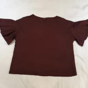 Mörkbrun top från Uniqlo - Brun, röd, lila, nånstans där, nästan skimrande.  Köpt i Japan. Storlek på lappen är L men kan liknas vid lös M.  Volang i ärmarna. 