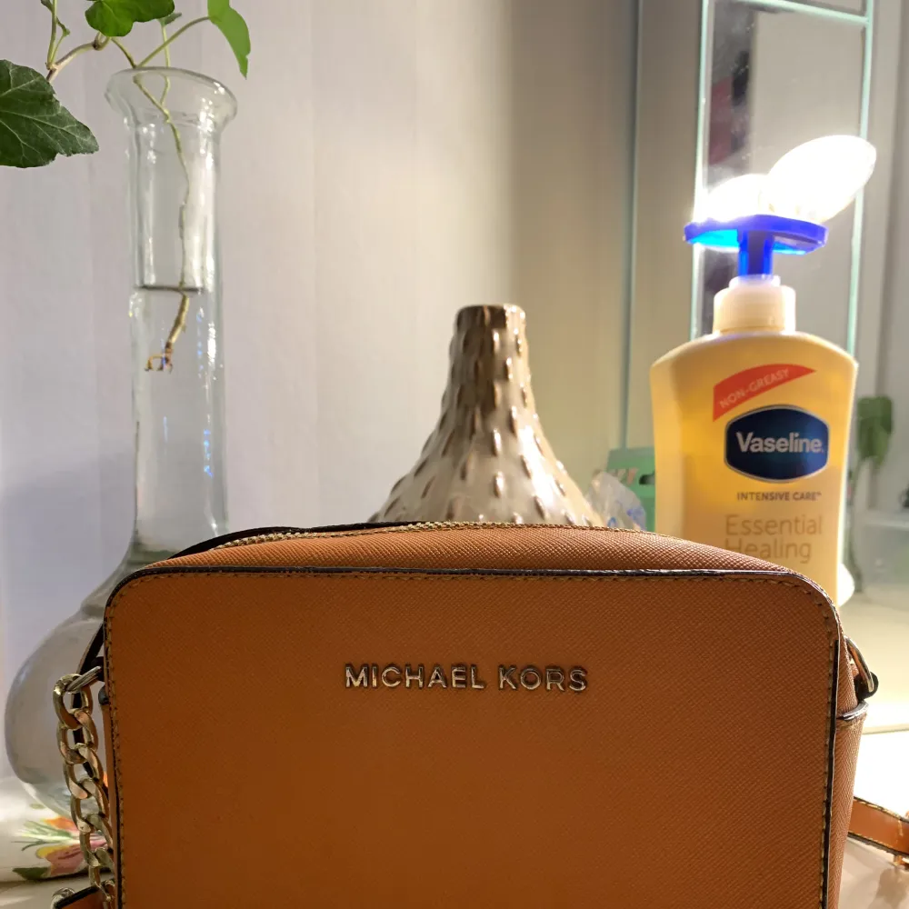Lite handväska som är orange, med långt band som man kan ha på axeln eller runt om. Väskor.