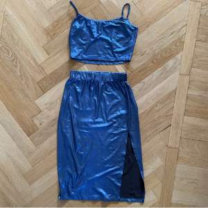 Topp + kjol i metallisk blå. Båda superstretchiga och mjuka, använda ett fåtal gånger. Kjolen är midi med slit. 