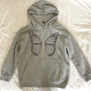 Zip hoodie - Populär grå zip up hoodie från shein med en fjäril på. Använd få gånger, inga defekter och är i nyskick. Köpt för 219kr men säljer för 50kr.