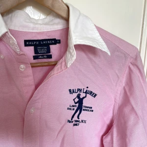 Ralph Lauren skjorta - Rosa Ralph Lauren Lawn Tennis N.Y 1967 skjorta. Passar storlek S / M Köpt second hand, men den är i perfekt skick förutom att det står ”Svensson” på insidan (syns inte alls på utsidan!!) 😇