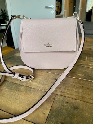 Kate Spade väska  - Oanvänd Kate Spade väska.Ljusrosa läder.Strl 20x17 cm.Kan skicka,då betalar mottagaren frakten på 69kr.