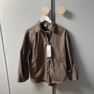 Arket skjorta i strl S i nyskick!  - Oanvänd poplinskjorta från Arket i en brun fin färg. I mycket gott skick, endast provad. Nypris 790kr