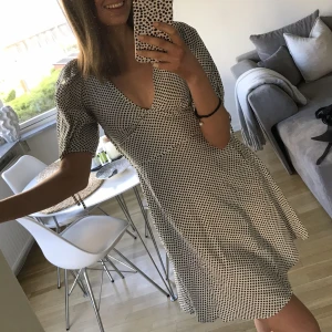 Prickig klänning - Prickig klänning från H&M i ljus beige/grå och svarta prickar. Knytningar vid ärmarna och dragkedja i midjan.  