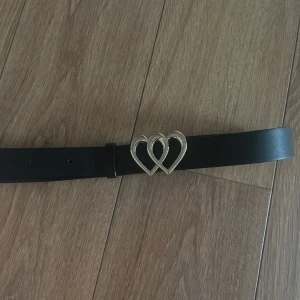 Svart fint skärp med guld detalj - Säljer mitt svarta skärp med två fina ”ihopsatta” guldhjärtan som bara är testad😊🫶 Storlek 70💗