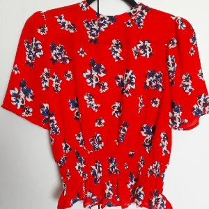 Somrig blus - Fin somrig röd blus med blåa blommor och smock nertill🌷 använd fåtal gånger!