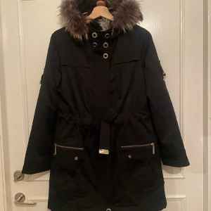 Vinterjacka - Paola Frani - En superfin vinterjacka med faux fur foder inuti och knyt i midjan. Pälsfodret inuti är avtagbart och även luvan och pälsen på luvan är avtagbar. Jackan är inköpt för 10.000kr från märket Paola Frani och är väl omhändertagen.