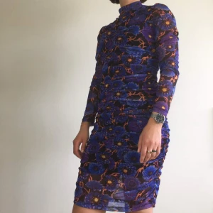 Mönstrad draperad mesh-klänning - Rush mesh multi-färgad från Junkyard. Underklänning i svart stretchigt tyg ingår i klänningen, som annars är i lite genomskinlig mesh. Denna är i nyskick, inte använd alls. 