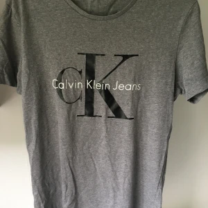 Calvin Klein t-shirt - Grå Calvin Klein t-shirt. Liten spricka på en av bokstäverna (se bild).  I övrigt fint skick. 