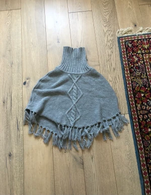 Stickad poncho  - En grå stickad poncho i storlek 158/170 barn. Väldigt fint skick, använd få gånger. Säljer för att jag aldrig använder plus att den är för liten för mig. Ny pris 200 kr. Super kön att ha en kall vinterdag, köparen står för frakten. 😊