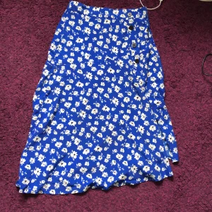 Blå långkjol - Blommig, marinblå långkjol med slits! Knappar, högmidjad från bershka! Har en liten skråma 🩷priv 🩷 superskön och somrig 😘pris diskuterbart. Sätter långkjol på frakten men den blir mindre när man viker den 🤷🏼‍♀️💞liten i strl