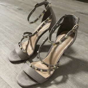 Grå klackskor strl 36 - Säljer dess ljusgråa klackskor i stl 36. Aldrig använda. En nit har dock lossnat men inget man tänker på. (Se bild)