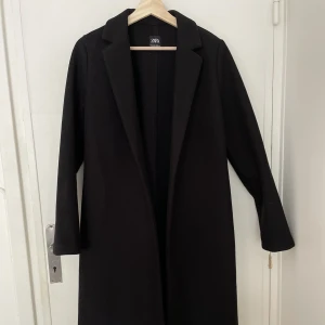 Svart kappa - Svart höst/vårkappa från Zara. Jag är 170cm och den når precis ner till knäna. Använd färre än 5 gånger så nyskick. Storlek M men lite smal i armar/axlar. Har bra fickor