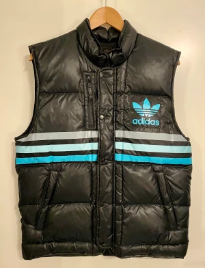 Adidas dunväst stl S - Svart Adidas väst, storlek S men passar även M. Bra skick, några repor i trycket på de tre ränderna förekommer. Mått mellan ärmhålor: ca 52 cm