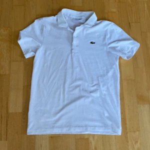 Lacoste piké  - Sjysst vit Lacoste piké som ej kommer till användning, köpte på flygplatsen på resa i våras men använder den inte så mycket längre, priset går att diskutera så det är bara att höra av sig vid frågor.