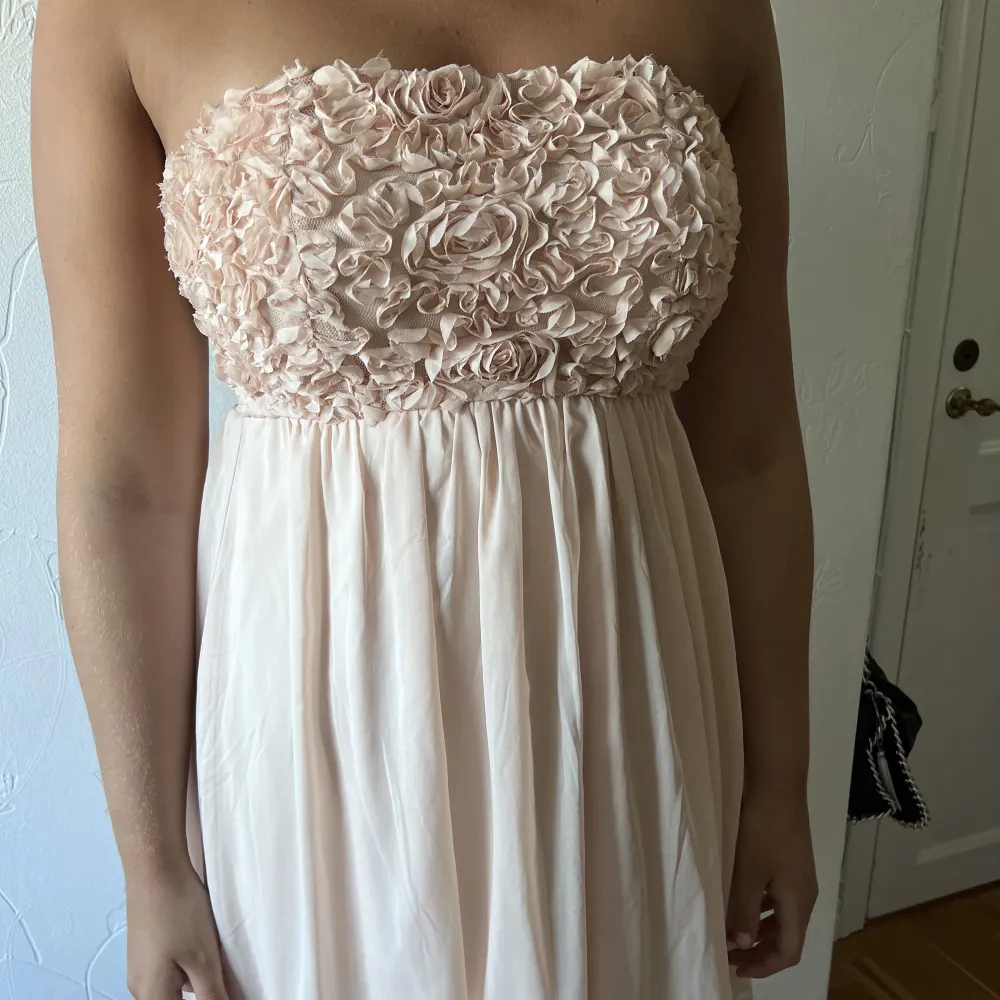 En rosa klänning med ”blommor” på bröstet. Finns axelband till. Klänningar.