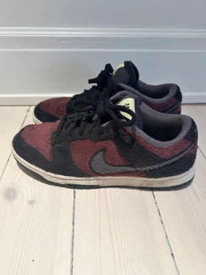 Säljer äkta NIKE Dunk Low SE - 1 par NIKE Dunk Low SE Storlek EU 38 / US 7 Färg svart och vinrött, mjukt tyg Fint skick, sparsamt använda, se bilder.