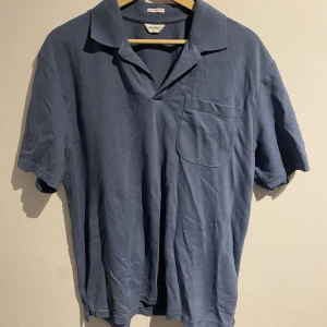 East West piké - Piké i en mörkblå timmen en bröst ficka. Materialet har lite textur. 100% bomull