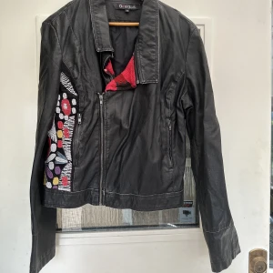 Skinnjacka Desigual - En kort skinnjacka med broderat på ena sidan. Mjukt läder