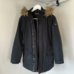 Vinterjacka Tommy Hilfiger - Högkvalitativ vinterjacka med luva från Tommy Hilfiger. Bra skick, någon enstaka repa eller fläck men utöver det är den som ny. Säljer pga för liten storlek. Hör av dig om du har frågor! Nypris 2 500kr.