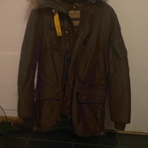 Parajumper herr - Brun, kraftig dunjacka från Parajumpers med flera praktiska framfickor och en innerficka med dragkedja.Jackan har även ett avtagbart dunfoder.Jackan har en snygg avtagbar krage i naturpäls runt luvan samt det ikoniska gula kabinhaken.Dragkedja Stl stor M