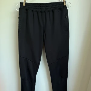 Mjukis/träningsbyxor - Mjukis/träningsbyxa i polyester med fickor med dragkedja och en kort dragkedja längst ner vid fötterna. 