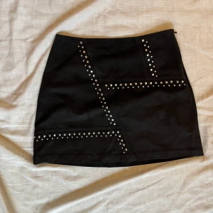 Svart minikjol  - Svart minikjol med detaljer framtill. Fejkmocka.