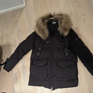 Cedrico dunjacka Gilbert M - Säljer min dunjacka från Cedrico modell Gilbert i storlek M pga att jag inte har den på mig mer. I fint skick utan hål eller fel. Använd sparsamt 1 vinter. Köpt för ca 2 år sedan. Avtagbar päls runt hals.   Nypris 5500kr