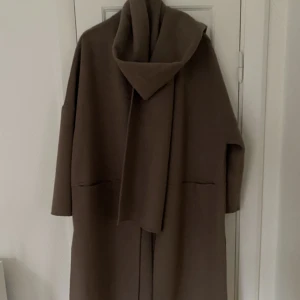 Kappa med halsduk  - Kappa från H&M i finare material. Rak modell som kommer med en avtagbar halsduk. Kappan är i en beige/brun färg och ser fin och lyxig ut! Använd fåtal gånger så är i fint skick. 